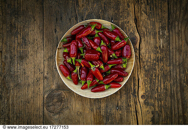Plate of fresh red chili peppers on wooden surface