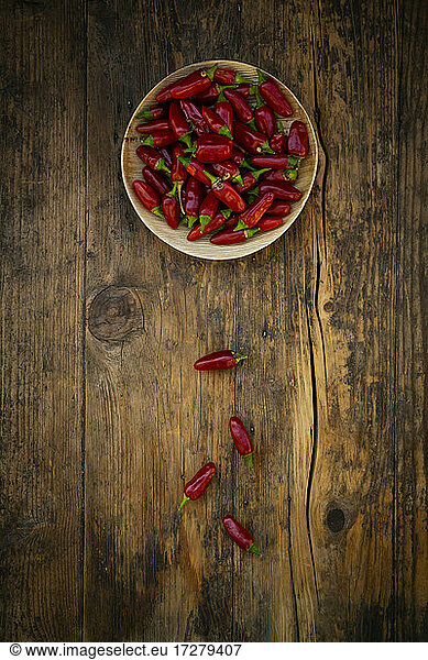 Plate of fresh red chili peppers on wooden surface