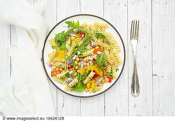 Plate of vegetarian pasta salad with chick-peas  bell pepper  arugula  onion  parsley and basil