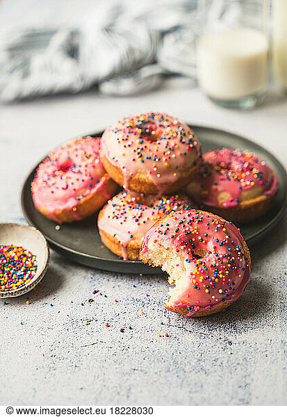 Plate of yummy vanilla cake donuts with pink icing and sprinkles.
