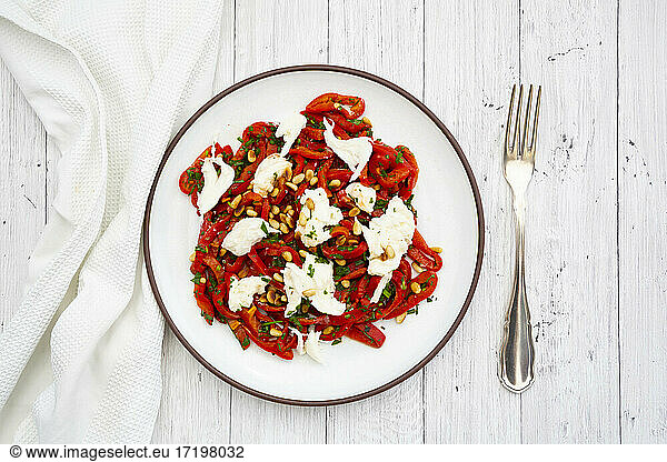 Plate with salad made out of pickled  roasted peppers with parsley  chives  mozzarella and roasted pine nuts
