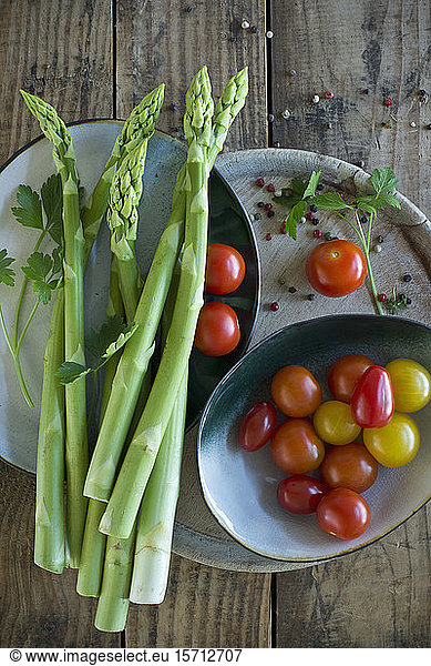 Plates and bowls with fresh cherry tomatoes  asparagus  parsley and pepper