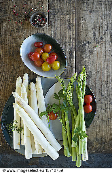 Plates and bowls with fresh cherry tomatoes  green and white asparagus  parsley  cress and pepper