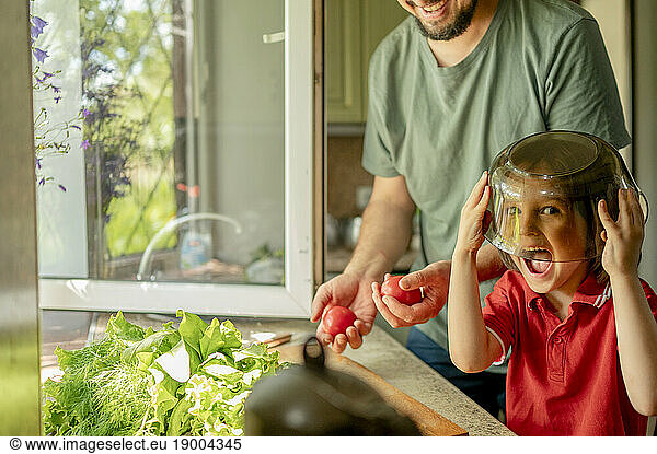 Playful boy covering face with bowl by father at home