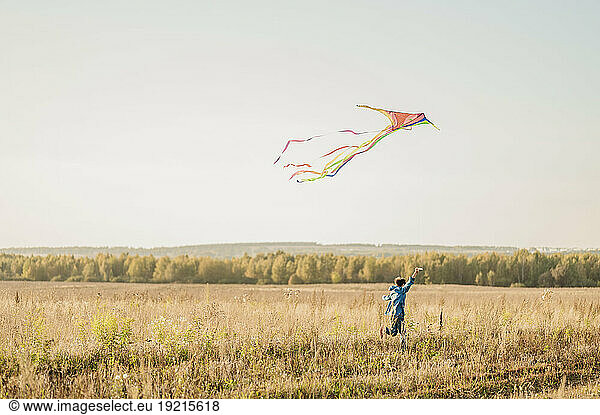 Playful boy flying kite in field