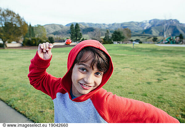 Playful boy holds his red lollipop and smiles at the camera