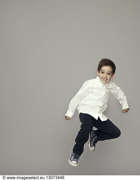 Playful boy jumping against gray background