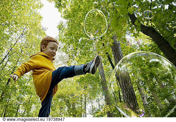 Playful boy kicking soap bubbles in autumn forest