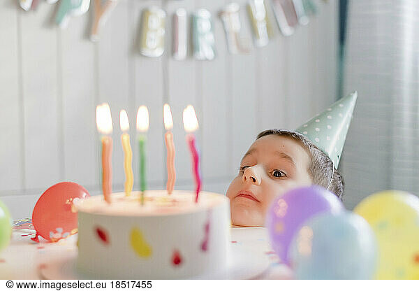 Playful boy looking at birthday cake with candles