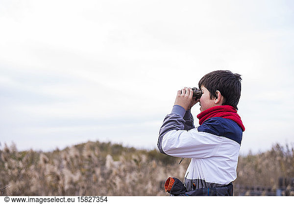 Playful boy looking through binoculars while standing on path