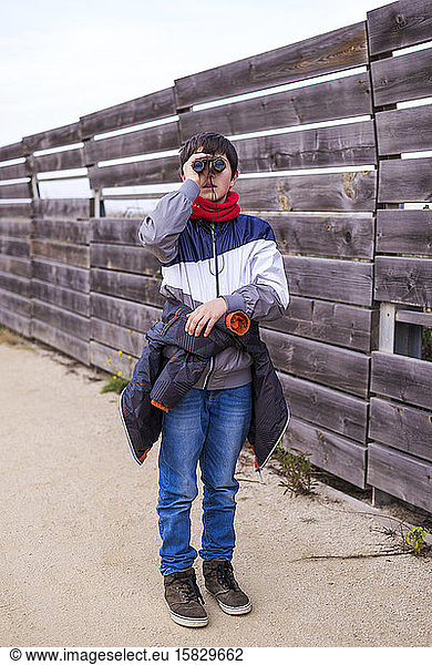 Playful boy looking through binoculars while standing on path