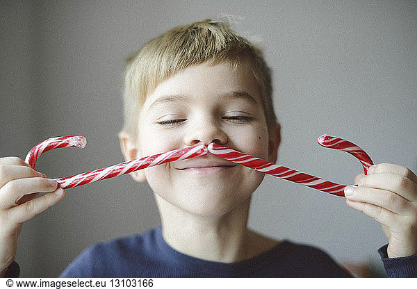 Playful boy making mustache with candy canes at home