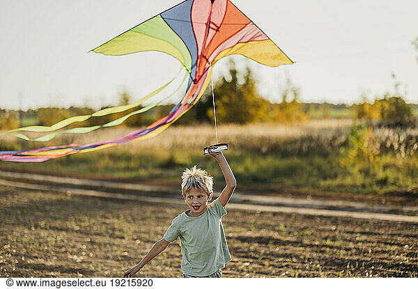 Playful boy running with multi colored kite in meadow