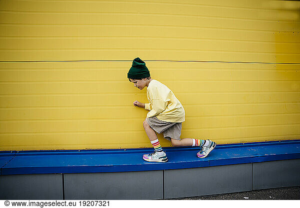 Playful boy wearing sweatshirt crouching in front of yellow wall