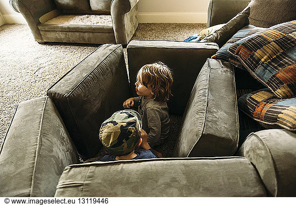 Playful boys hiding behind cushions at home