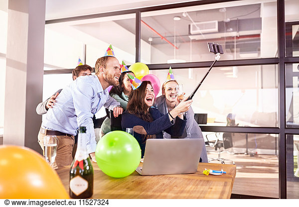 Playful business people celebrating birthday taking selfie with selfie stick in conference room