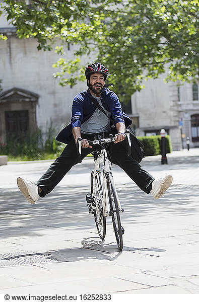 Playful businessman riding bicycle on sunny city sidewalk