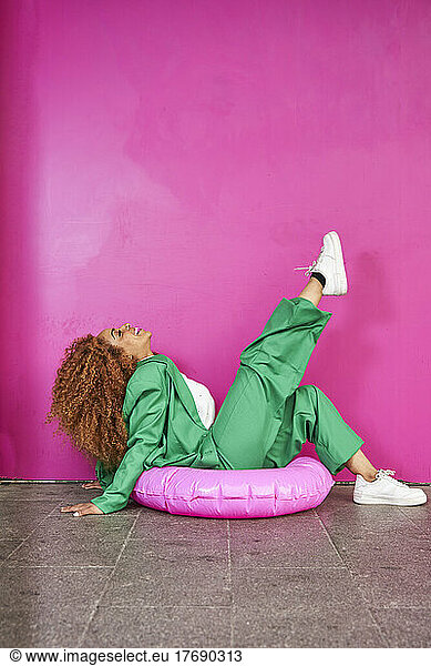 Playful businesswoman sitting on inflatable ring in front of pink wall