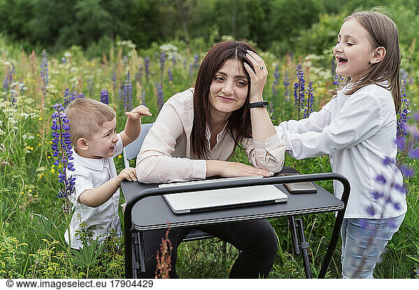 Playful children irritating mother sitting amidst lupine flowers