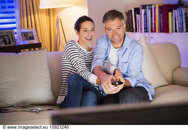Playful couple fighting over remote control watching TV in living room