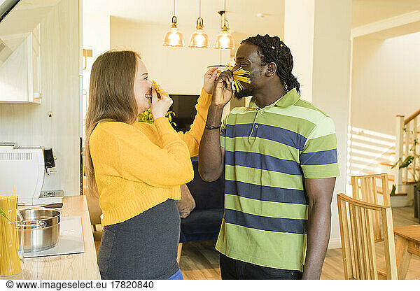 Playful couple making moustaches from uncooked spaghetti at home