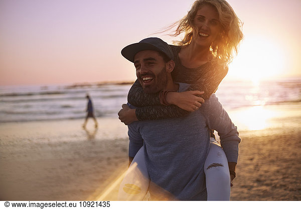 Playful couple piggybacking on sunset beach