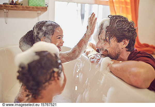 Playful daughters in bubble bath wiping bubbles on fatherâ€™s face
