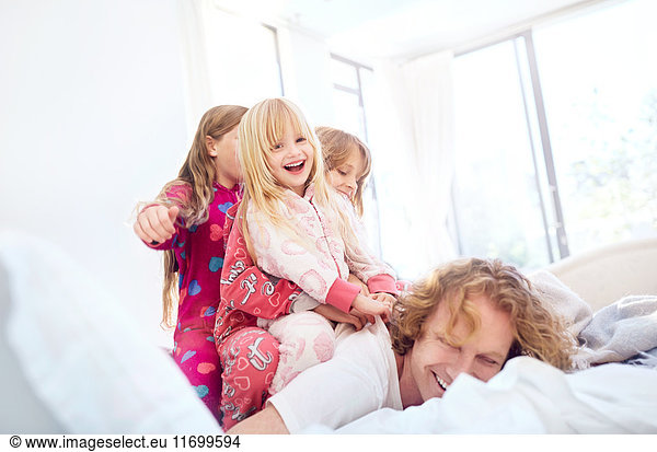 Playful daughters laying on top of father on bed