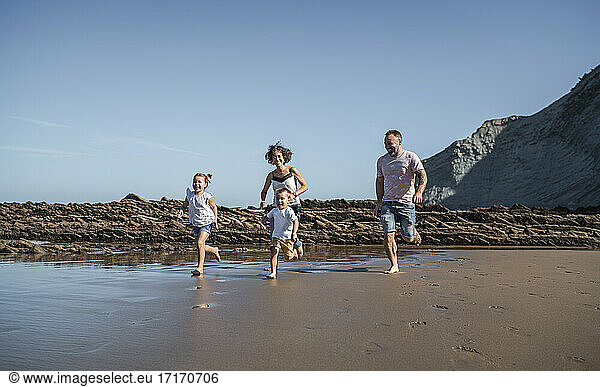 Playful family running at beach against blue sky