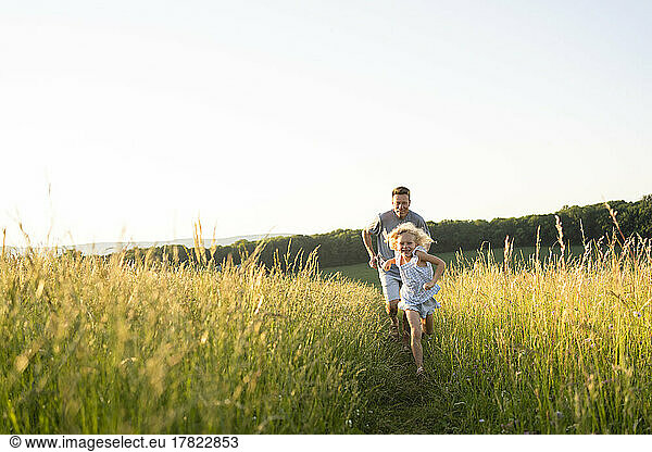 Playful father and daughter running in field