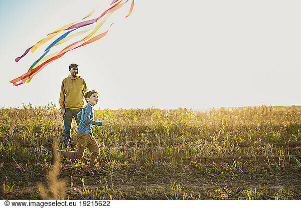 Playful father and son flying kite in field on sunny day