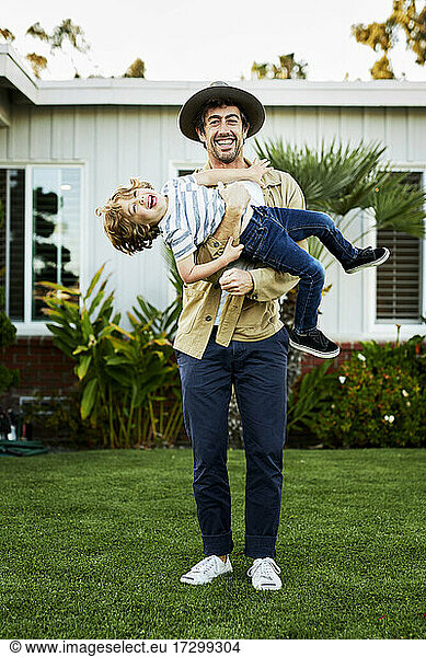 Playful father carrying happy son while standing in backyard