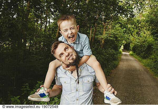Playful father carrying son on shoulder at forest