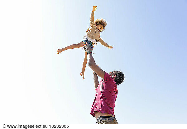 Playful father catching daughter under clear sky on sunny day
