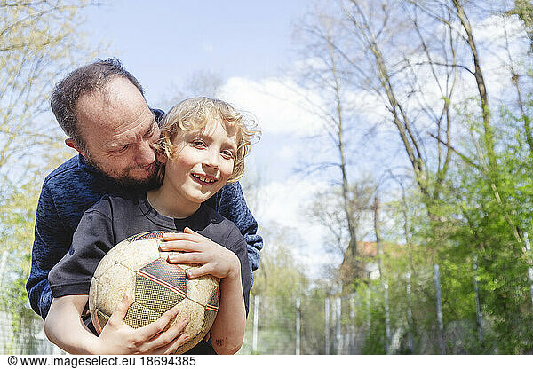 Playful father embracing smiling son holding soccer ball