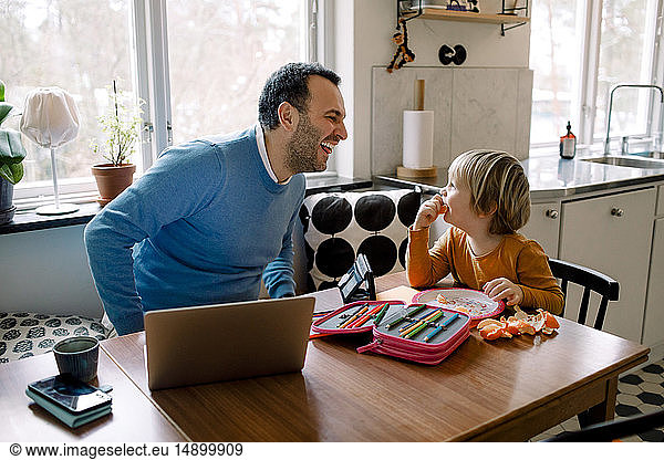 Playful father looking at daughter while using laptop at home