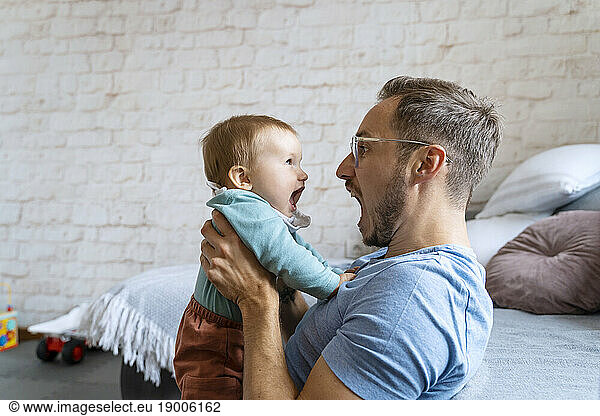 Playful father screaming with baby boy at home