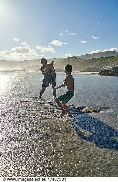 Playful father splashing son on sunny summer beach