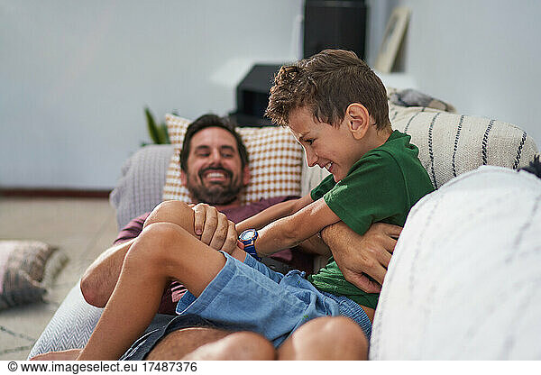 Playful father tickling son on living room sofa