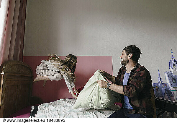 Playful father with daughter jumping on bed at home