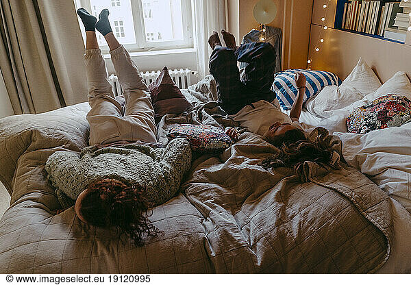 Playful female friends having fun while lying on bed at home