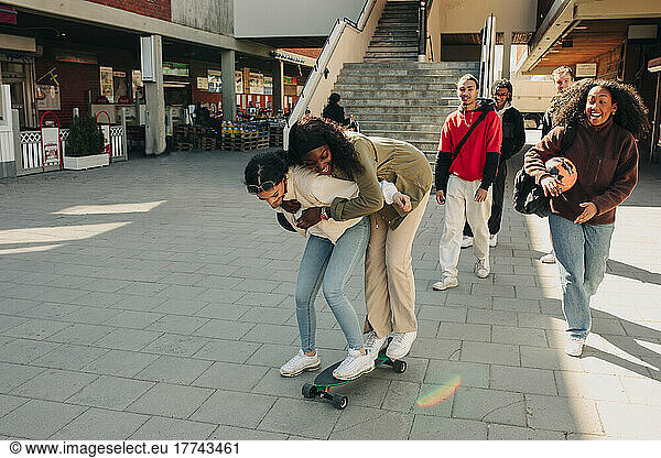 Playful female friends standing on skateboard at street