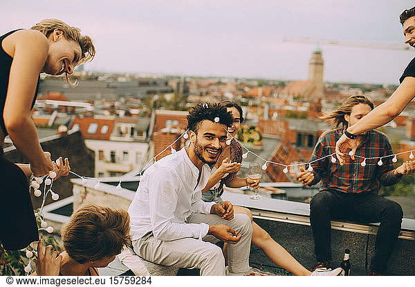 Playful friends enjoying with string light on terrace during rooftop party