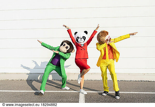 Playful friends wearing animal masks dancing in front of wall