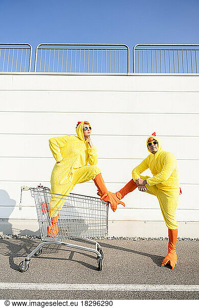 Playful friends wearing chicken costumes standing with shopping cart