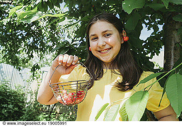 Playful girl holding cherry basket in garden