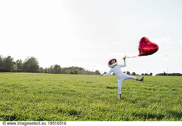 Playful girl holding heart shape balloon standing on grass