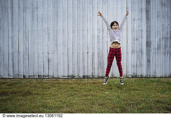Playful girl jumping against fence on field