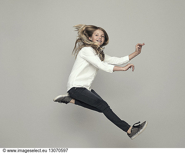 Playful girl jumping against gray background