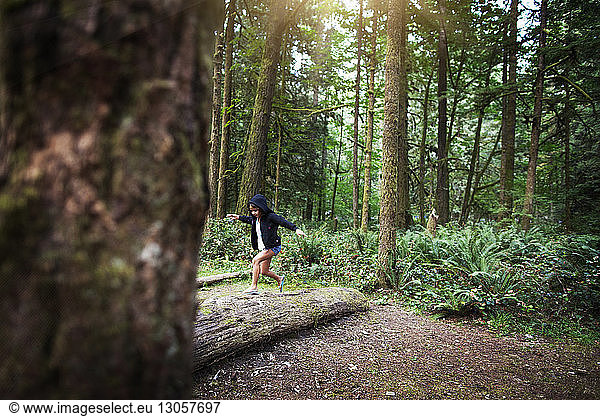 Playful girl running on fallen tree in forest